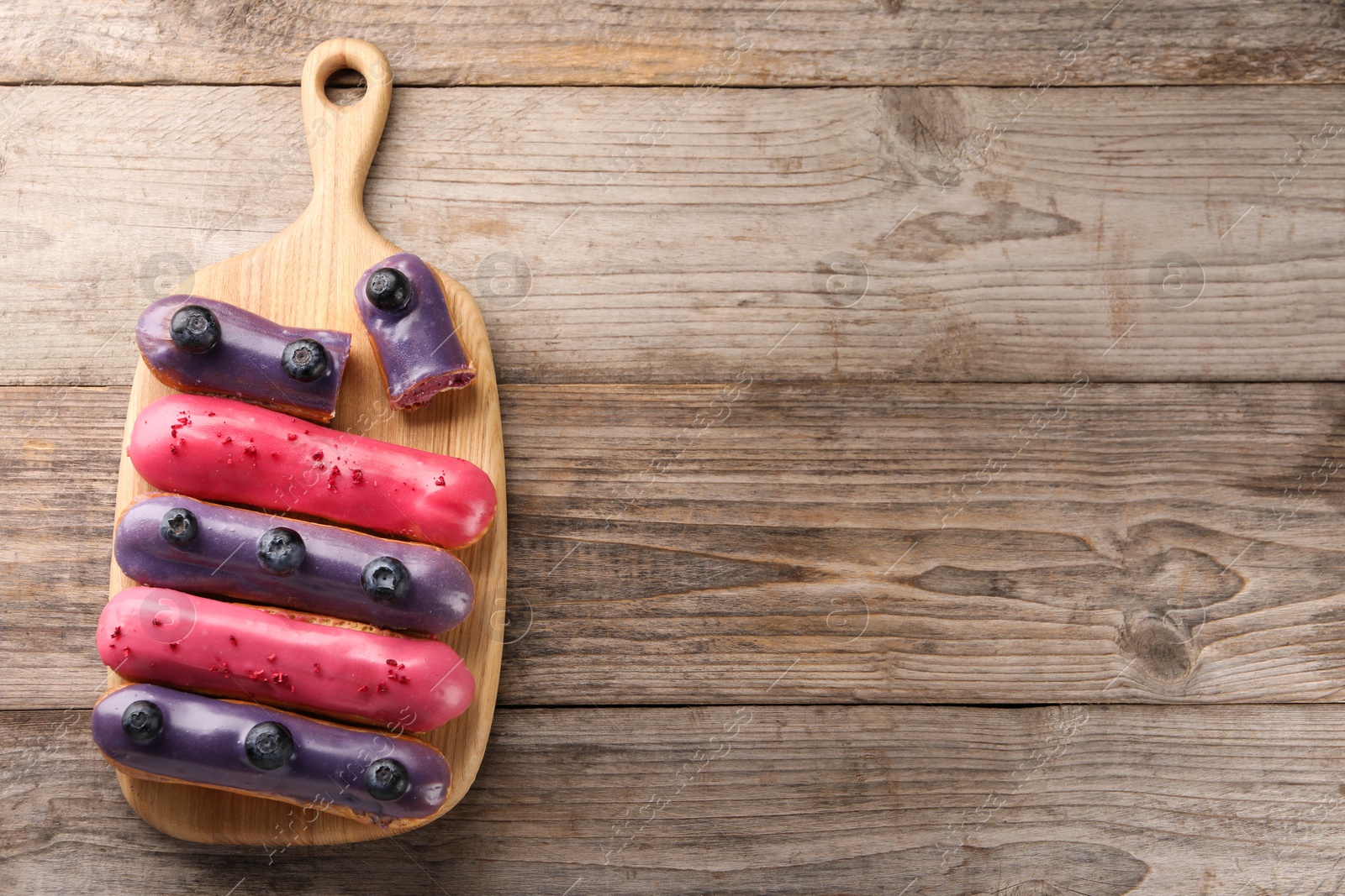 Photo of Different tasty glazed eclairs on wooden table, top view. Space for text