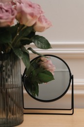 Mirror and vase with pink roses on wooden dressing table, closeup