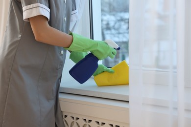 Photo of Chambermaid cleaning window sill with rag indoors, closeup