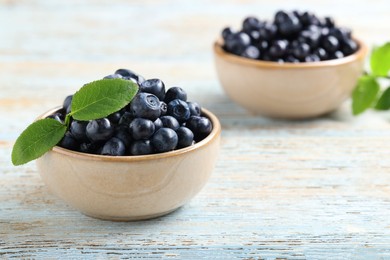 Photo of Tasty fresh bilberries with leaves on old light blue wooden table, space for text