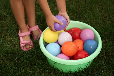 Photo of Little girl with basin of water bombs on green grass, closeup