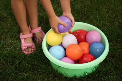 Little girl with basin of water bombs on green grass, closeup