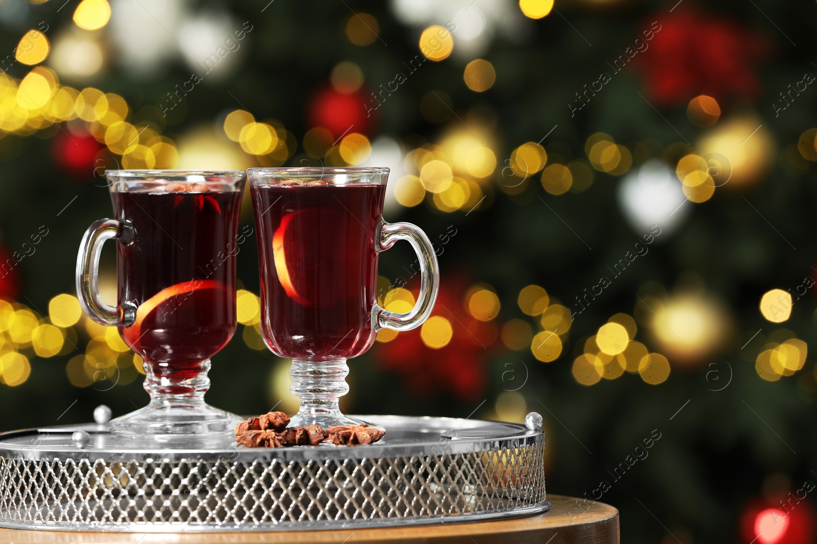 Photo of Hot mulled wine in glass cups and anise stars on table against blurred lights. Space for text