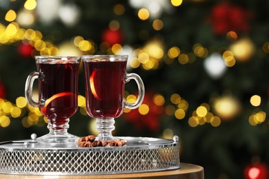 Photo of Hot mulled wine in glass cups and anise stars on table against blurred lights. Space for text