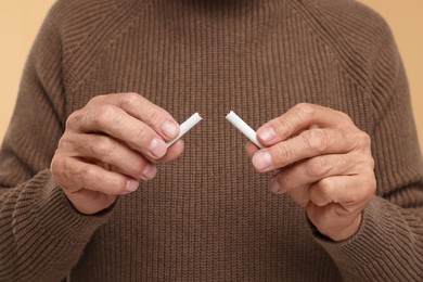 Photo of Stop smoking concept. Man holding pieces of broken cigarette on beige background, closeup