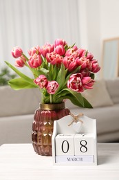 Photo of International Women's day - 8th of March. Block calendar and bouquet of beautiful tulips on white wooden table