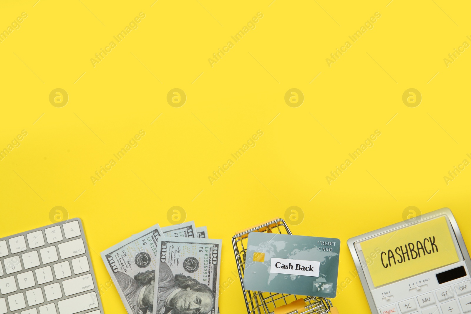 Photo of Calculator, keyboard, credit card, shopping cart and dollar banknotes on yellow background, flat lay with space for text. Cashback concept