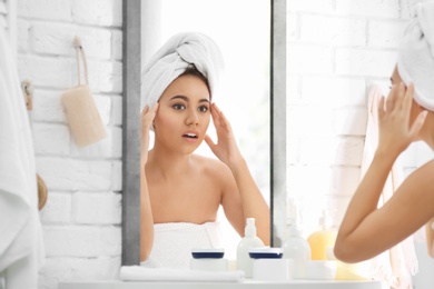 Beautiful young woman with acne problem looking in mirror at home