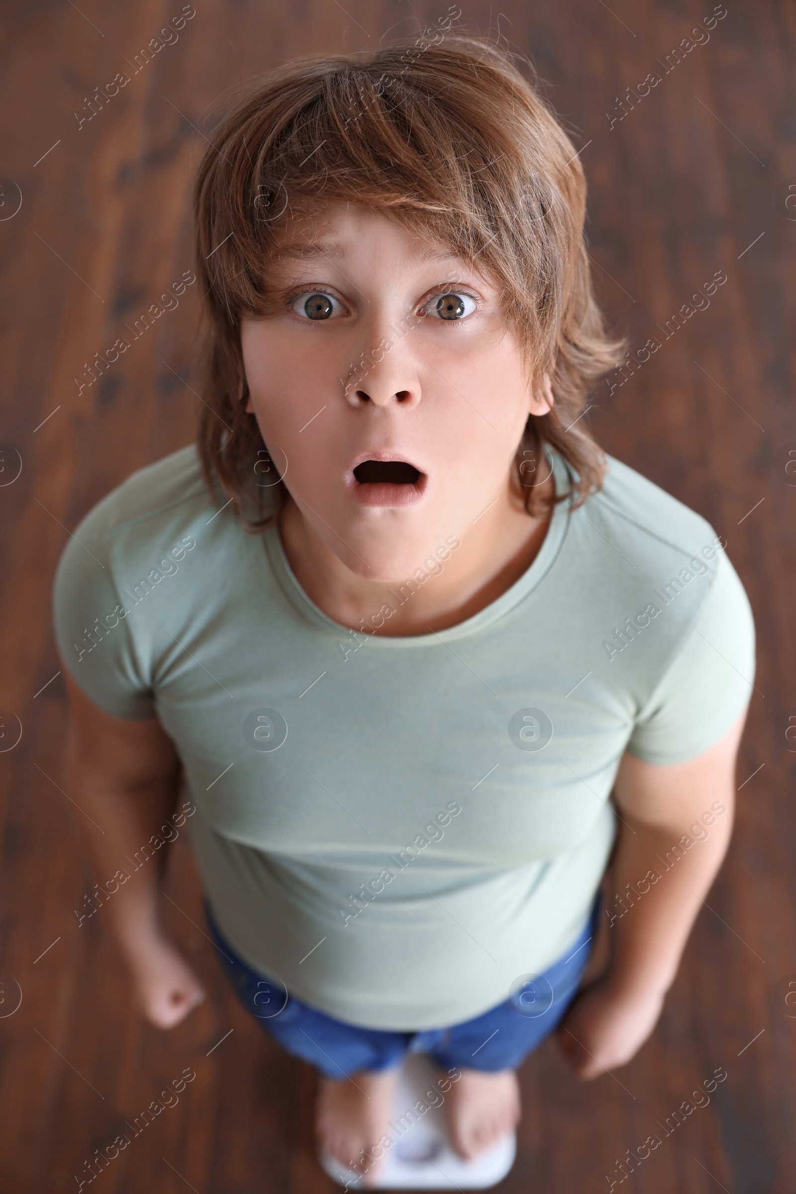 Photo of Emotional overweight boy standing on floor scales indoors, above view