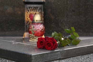 Photo of Red roses and grave light on grey granite tombstone outdoors, space for text. Funeral ceremony