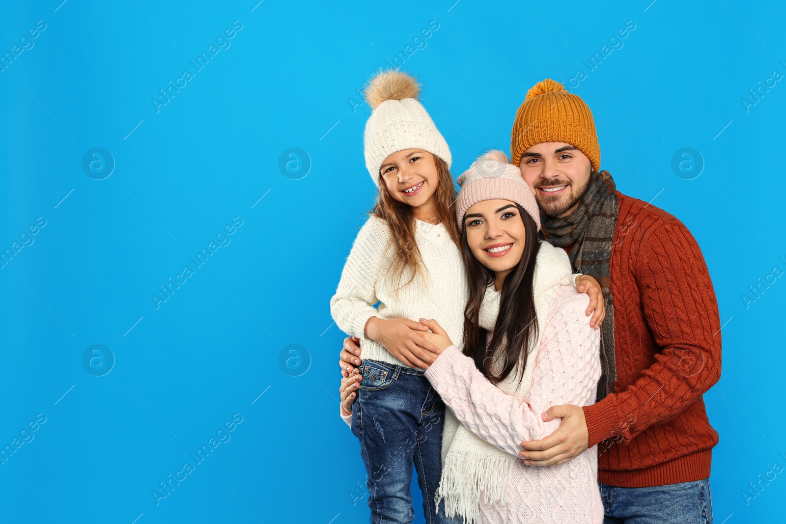 Photo of Happy family in warm clothes on blue background, space for text. Winter vacation