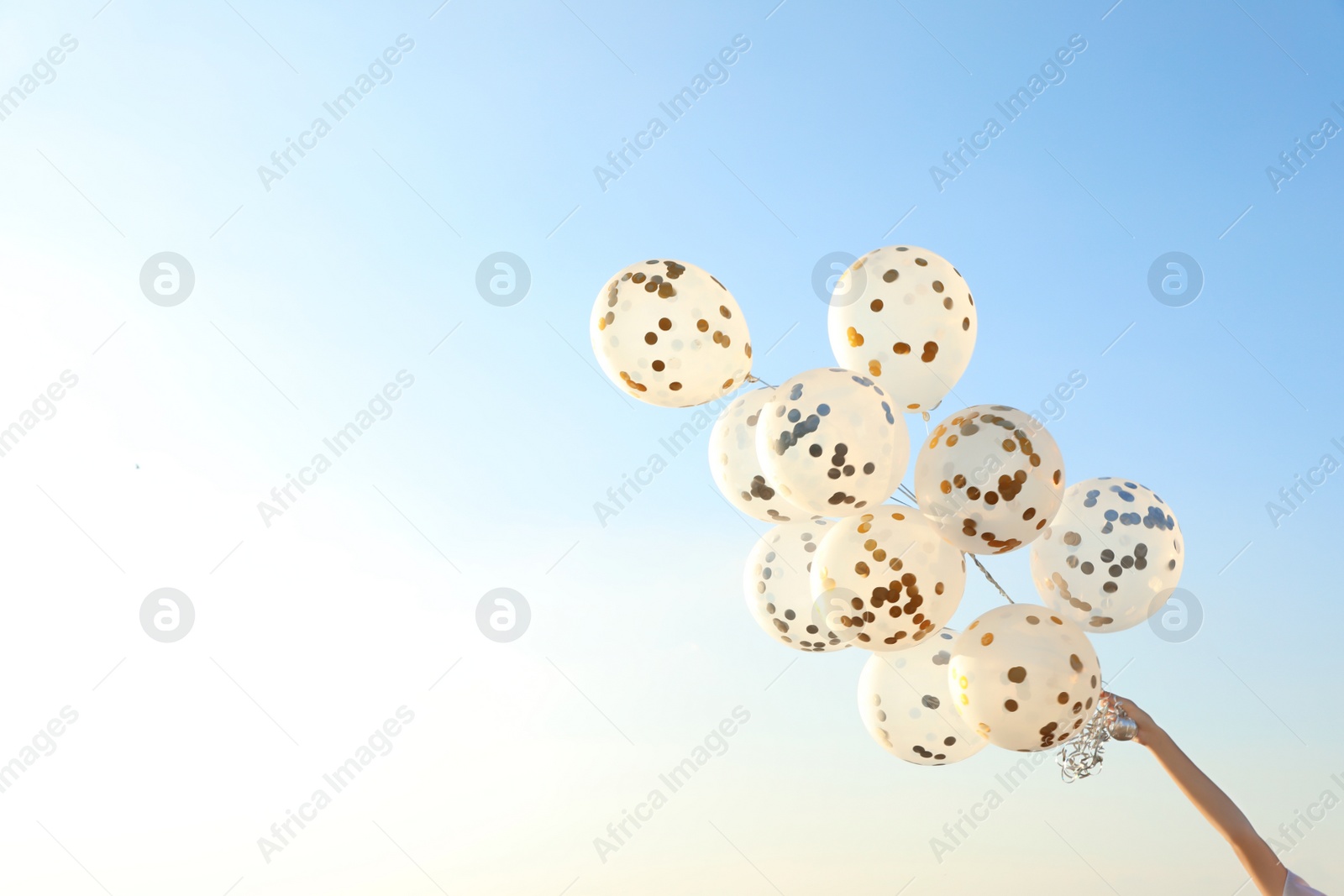 Photo of Young woman holding glitter balloons against clear blue sky. Space for text