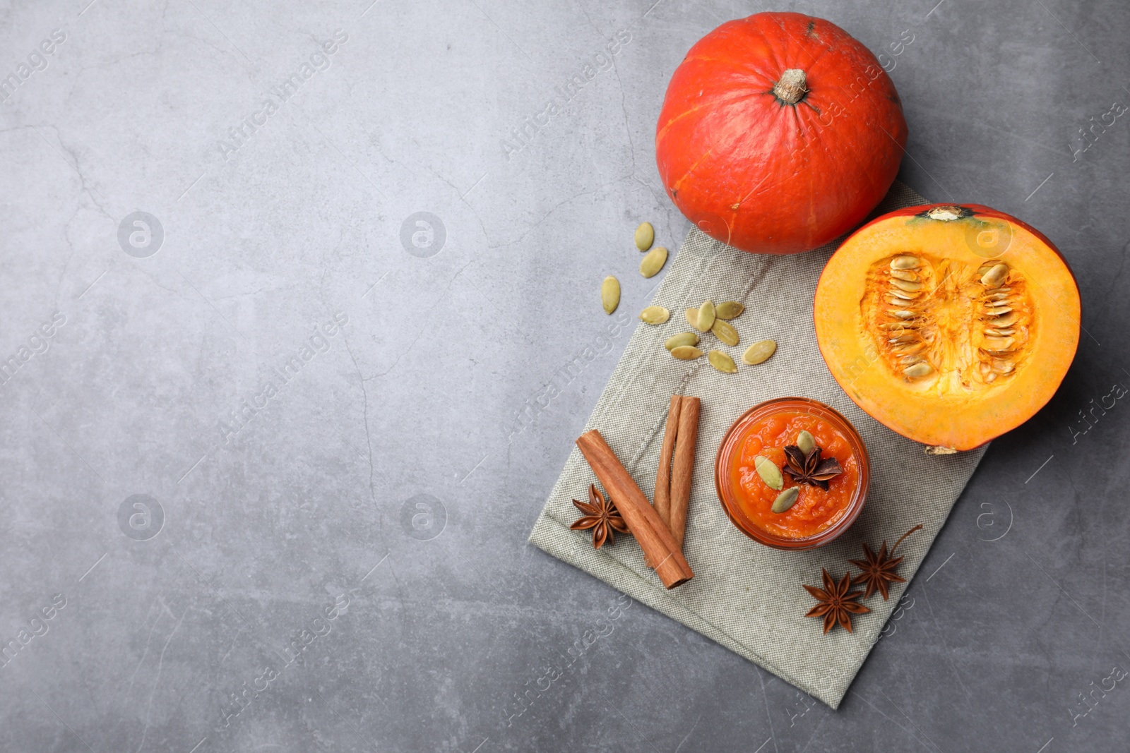 Photo of Jar of pumpkin jam, star anise, cinnamon and fresh pumpkins on grey table, flat lay. Space for text
