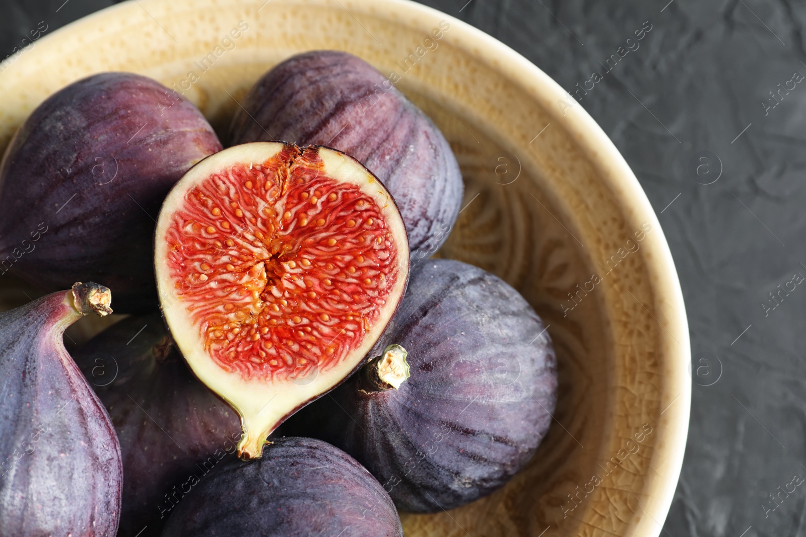 Photo of Bowl with fresh ripe figs on dark background, top view