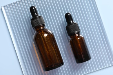 Bottles of cosmetic serum on light blue background, top view