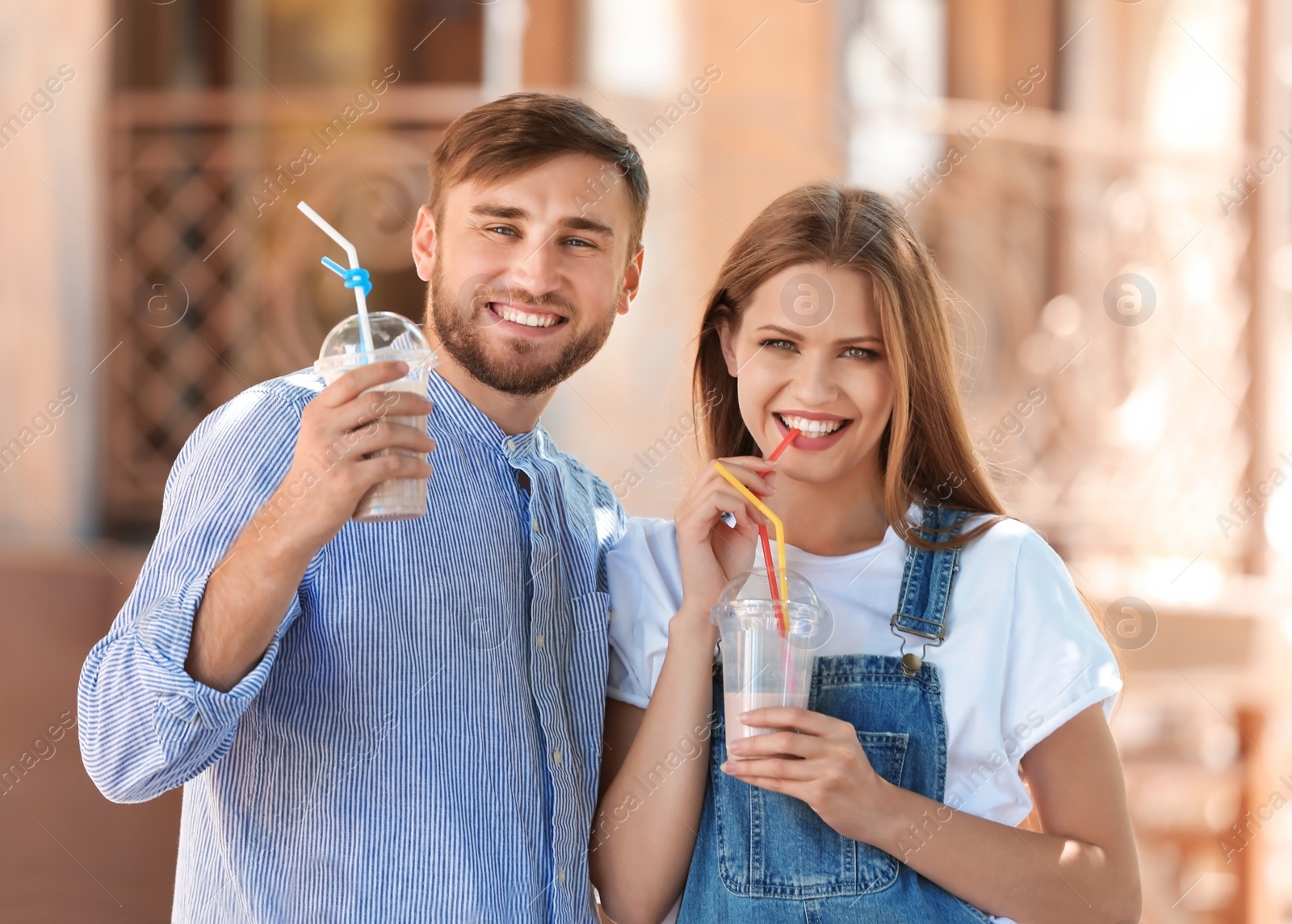 Photo of Young couple with cups of delicious milk shake outdoors