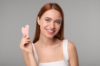 Photo of Young woman with rose quartz gua sha tool on grey background. Facial massage