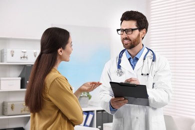 Photo of Doctor with clipboard consulting patient during appointment in clinic