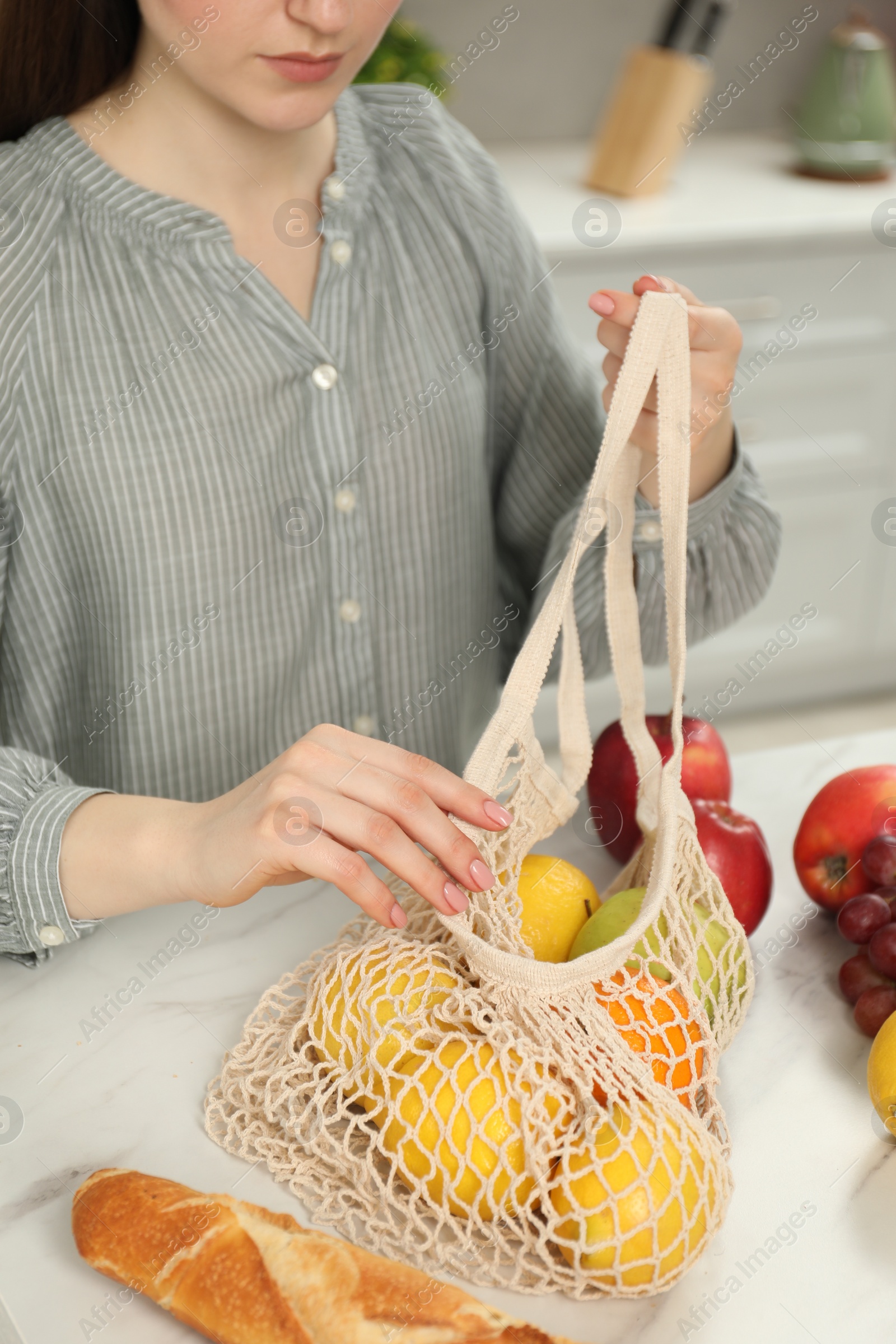 Photo of Woman with string bag of fresh fruits at light marble table, closeup