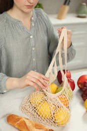 Woman with string bag of fresh fruits at light marble table, closeup