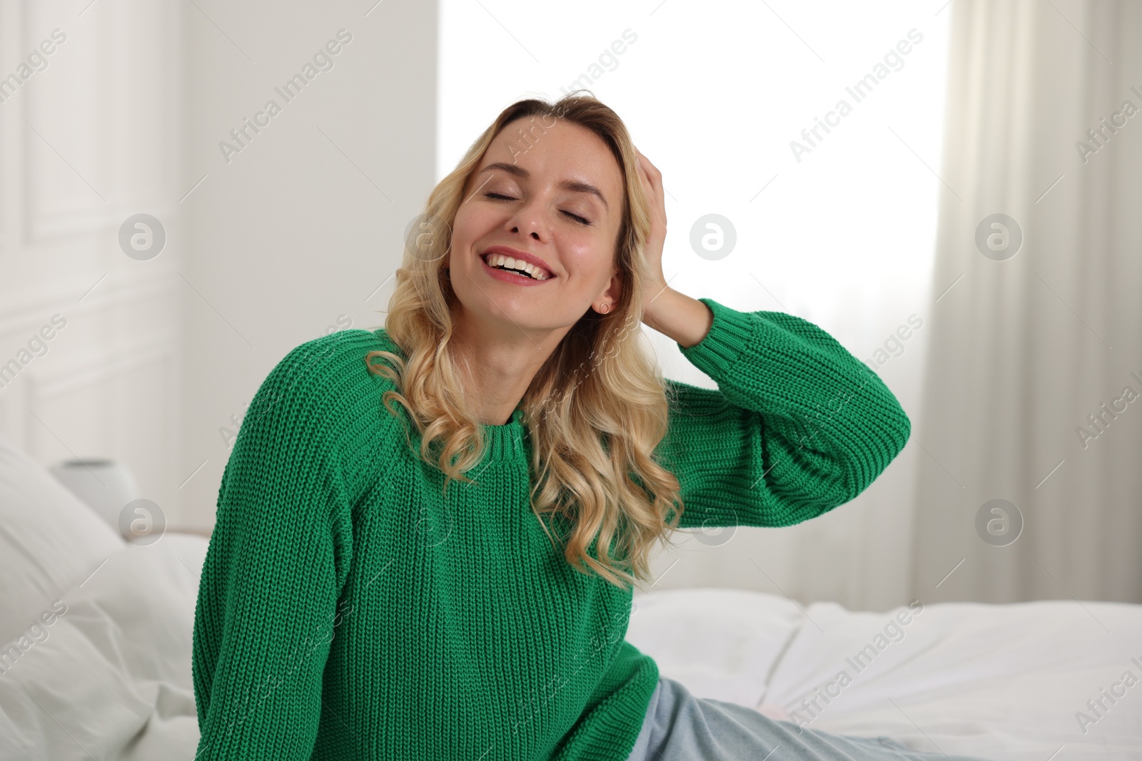 Photo of Happy woman in stylish warm sweater on bed at home