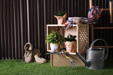 Beautiful plants, gardening tools and accessories on green grass near wood slat wall