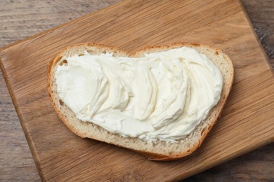 Photo of Slice of bread with tasty cream cheese on wooden table, top view