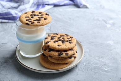 Photo of Delicious chocolate chip cookies and glass of milk on grey textured table, space for text