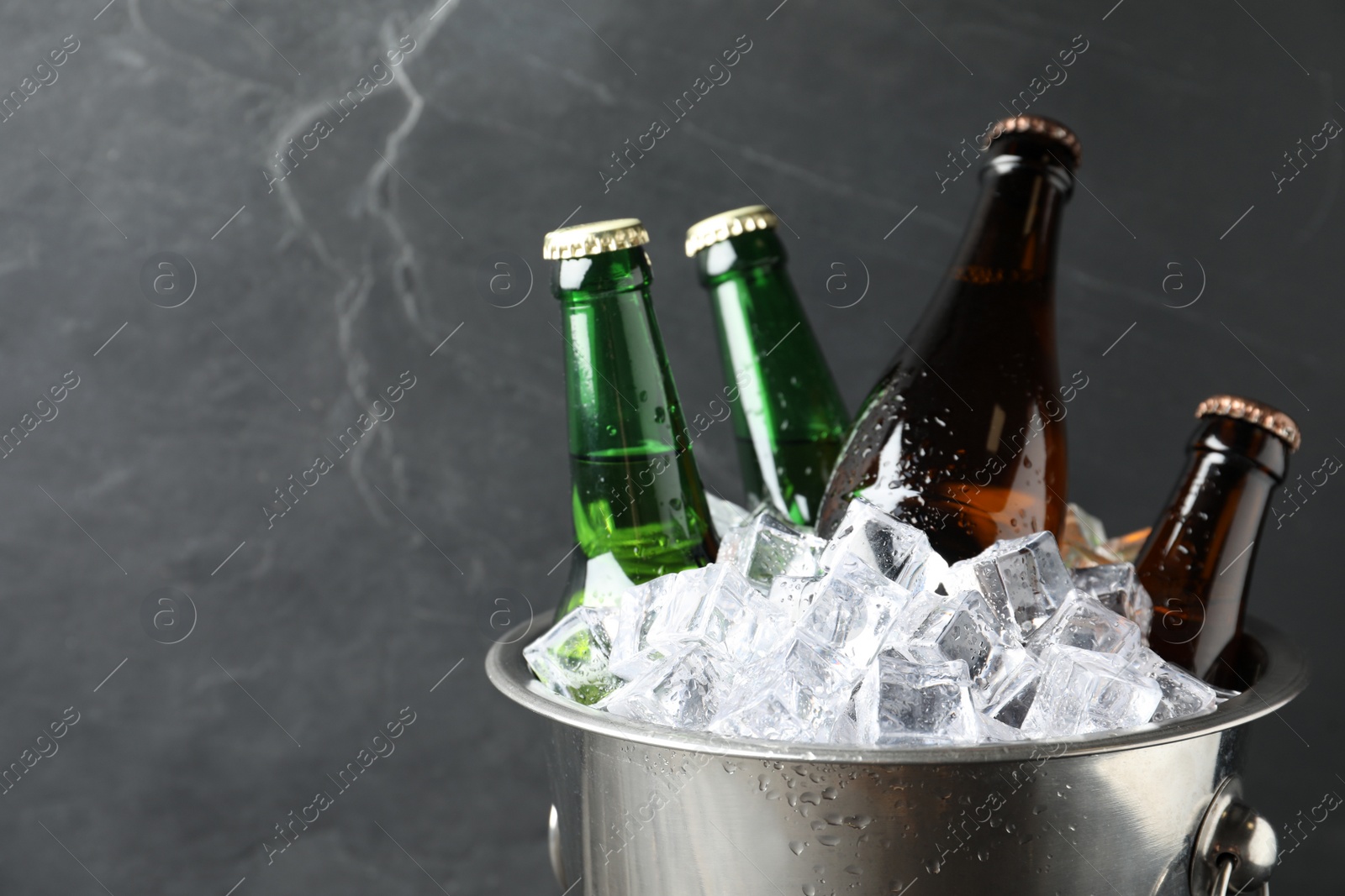 Photo of Metal bucket with beer and ice cubes on grey background, closeup. Space for text