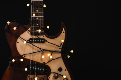Photo of Guitar with golden lights on black background, space for text. Christmas music