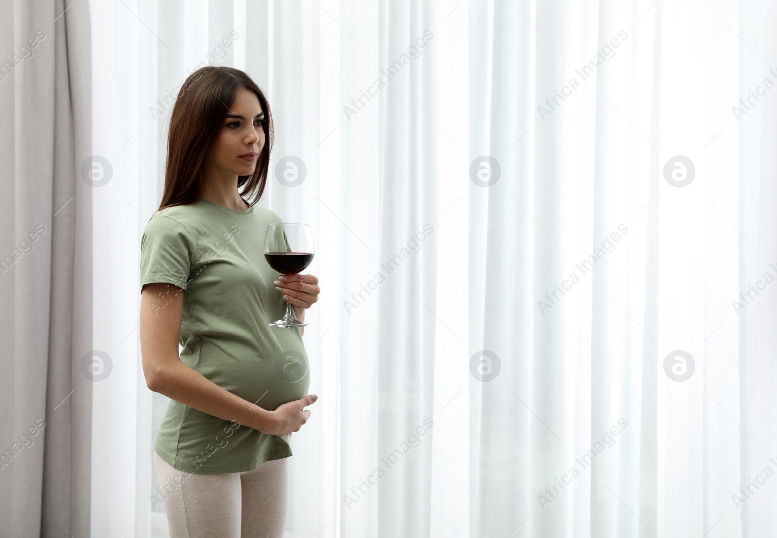 Photo of Pregnant woman with glass of wine indoors, space for text. Alcohol abuse during pregnancy