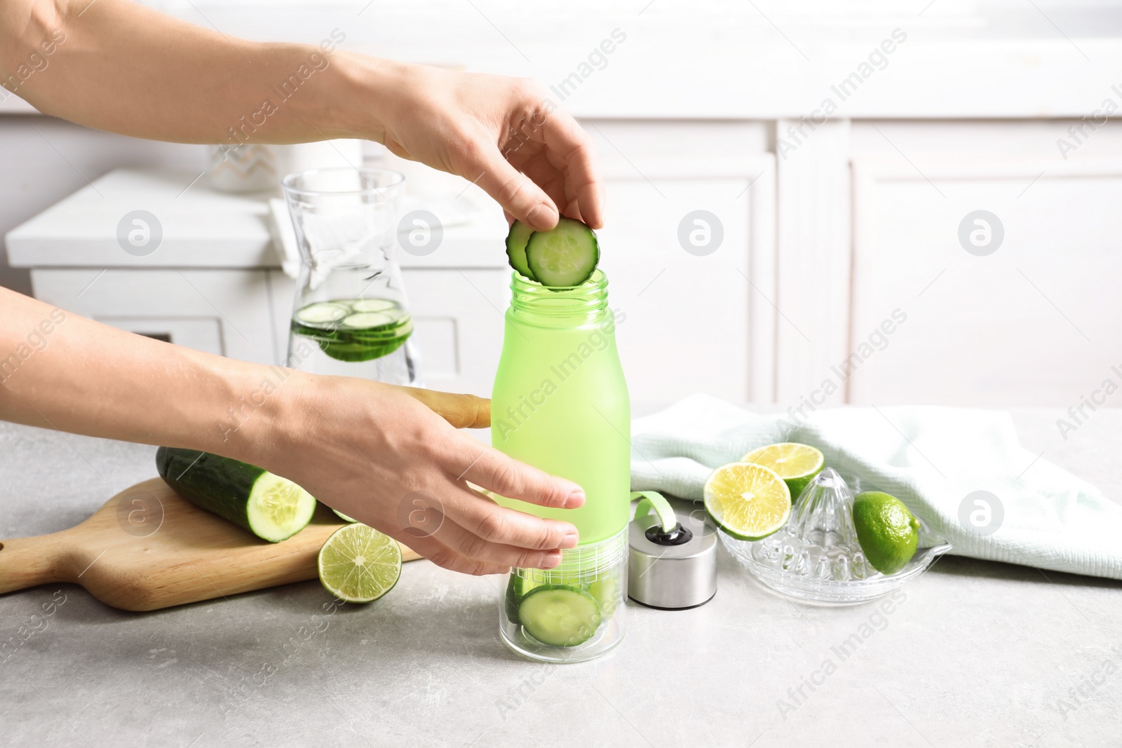 Photo of Young woman putting fresh cucumber slices into sports bottle on table. Space for text