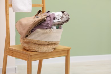 Photo of Laundry basket filled with clothes on chair in bathroom. Space for text