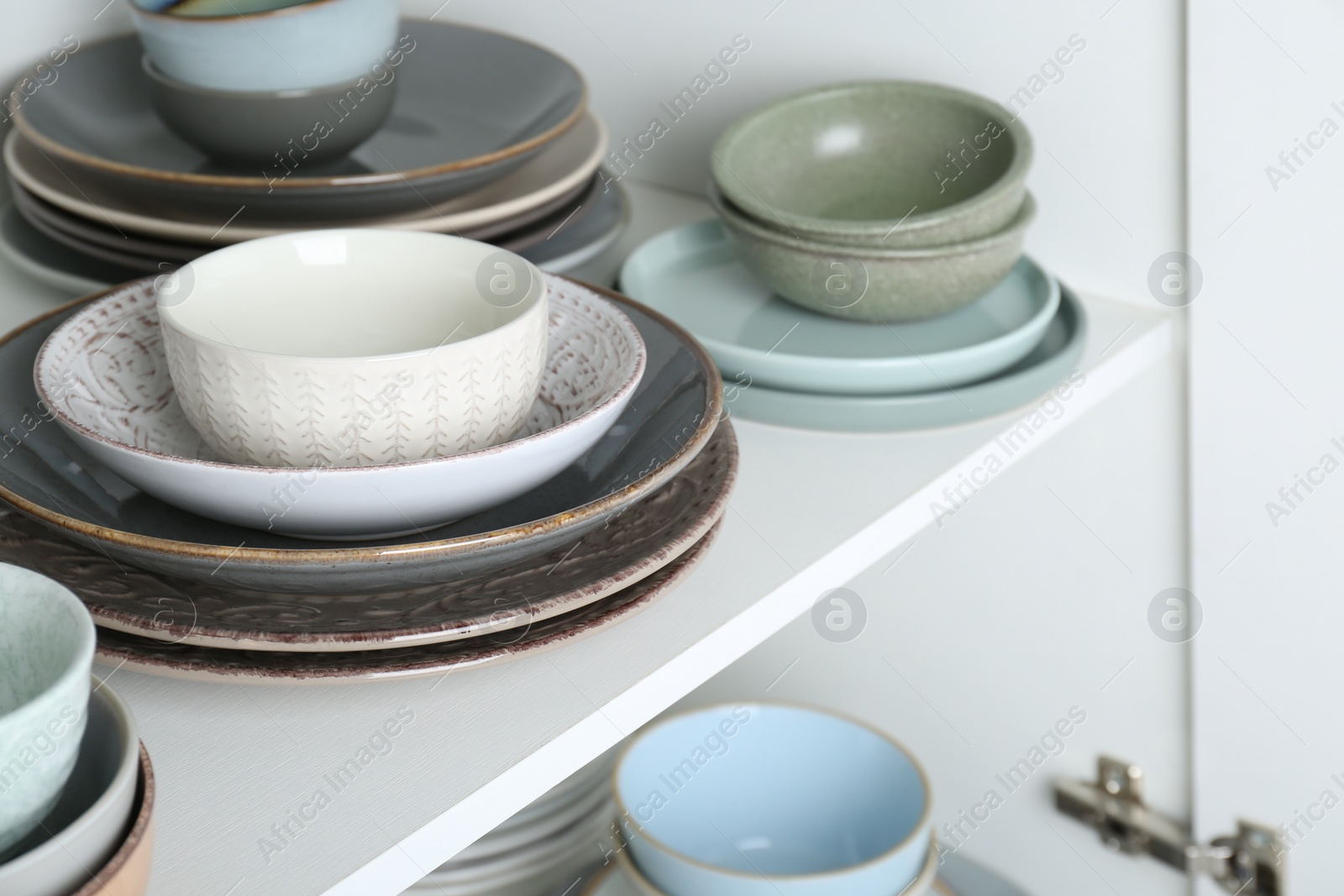 Photo of Different clean plates and bowls on shelf in cabinet, closeup