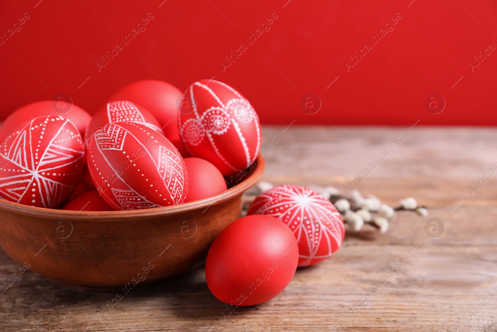 Photo of Wooden bowl with red painted Easter eggs on table against color background, space for text