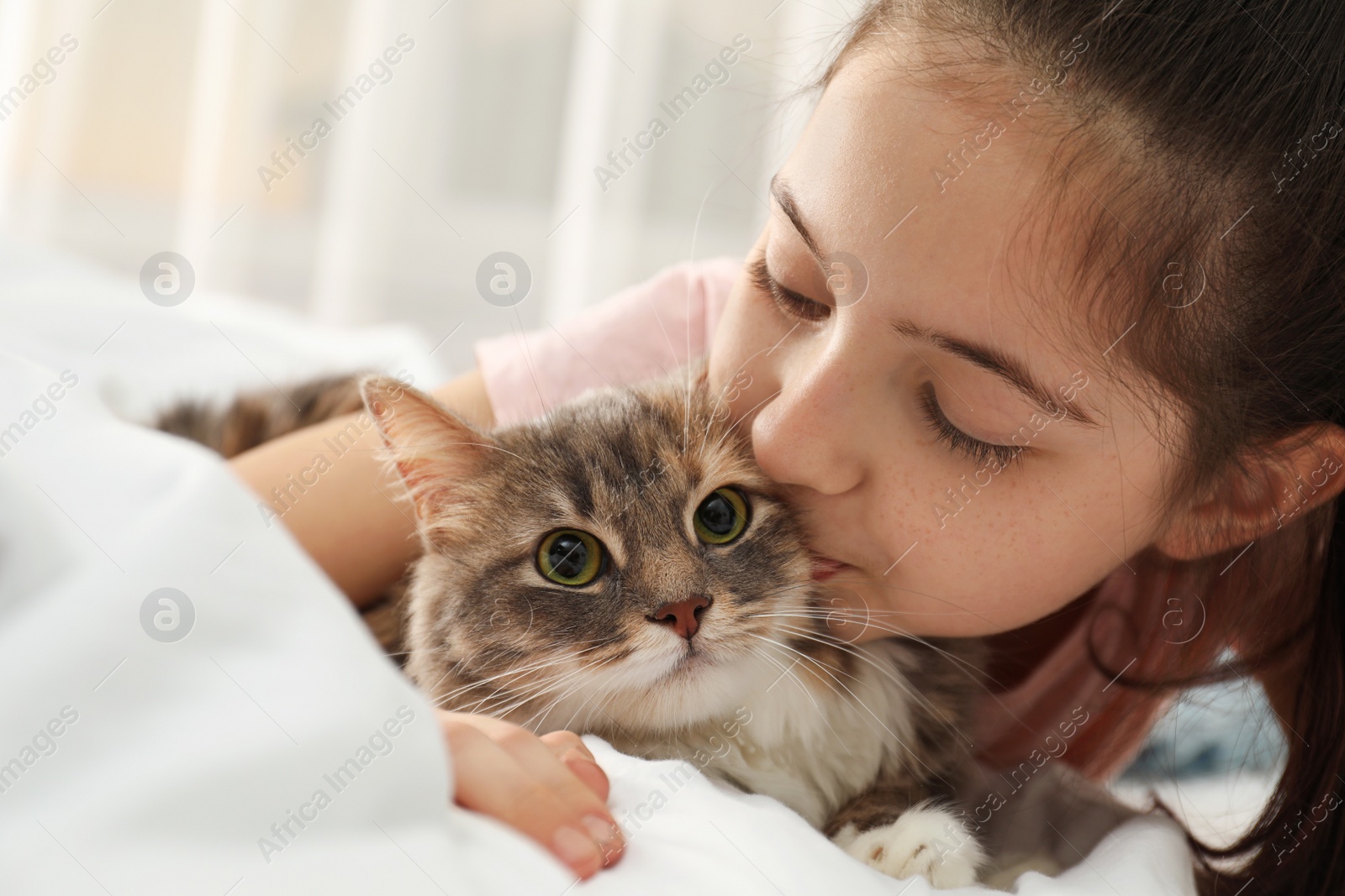 Photo of Cute little girl with cat lying on bed at home, closeup. First pet