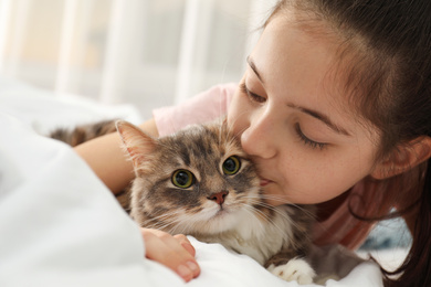 Cute little girl with cat lying on bed at home, closeup. First pet