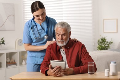 Photo of Young healthcare worker consulting senior man at wooden table indoors