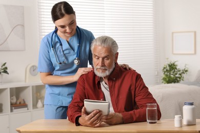 Young healthcare worker consulting senior man at wooden table indoors