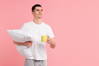 Photo of Happy man in pyjama holding pillow and cup of drink on pink background, space for text