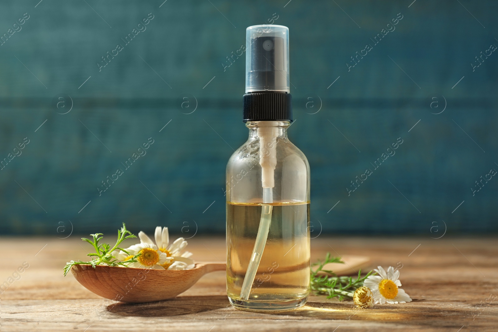 Photo of Bottle of chamomile essential oil and spoon with flowers on wooden table