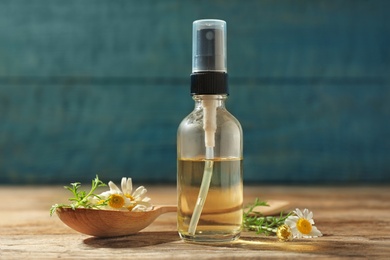 Photo of Bottle of chamomile essential oil and spoon with flowers on wooden table