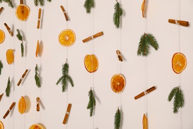 Handmade decor of dry orange slices, cinnamon sticks and fir tree branches on white wall, closeup