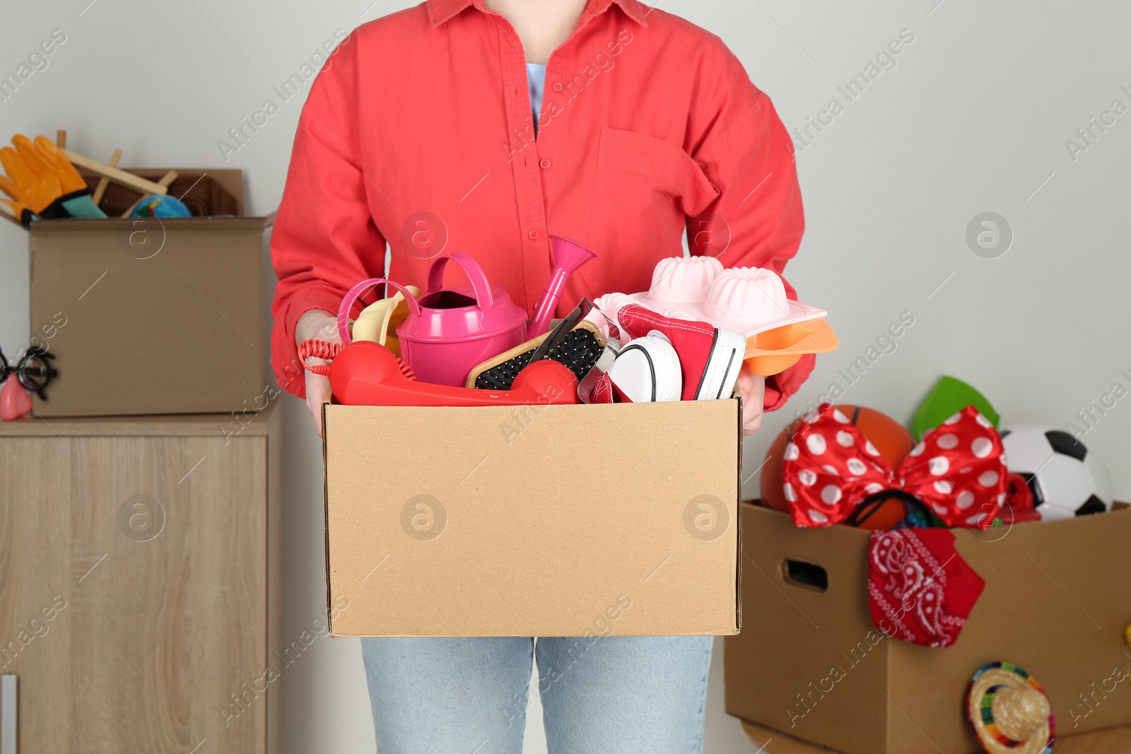 Photo of Woman holding box of unwanted stuff indoors, closeup