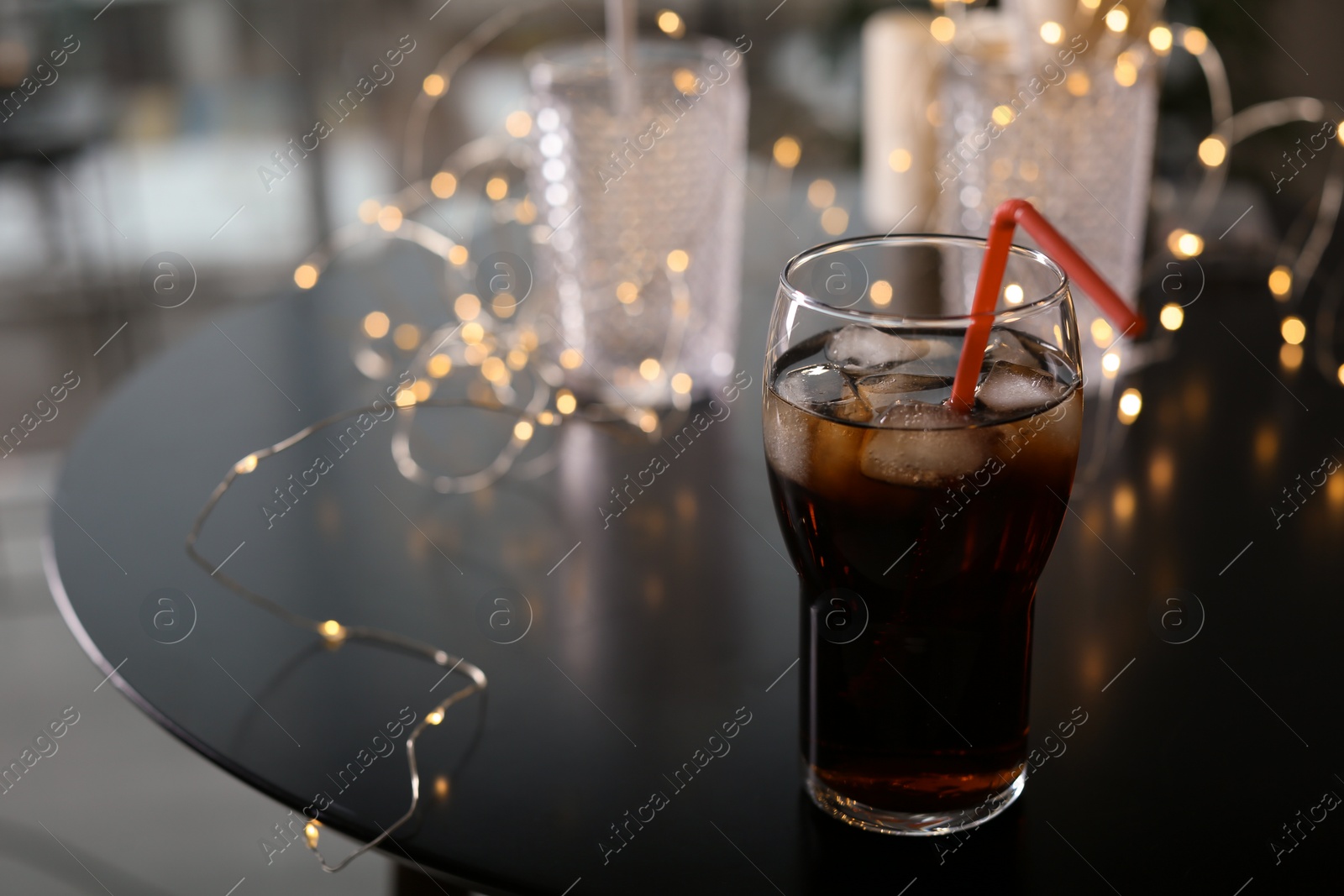 Photo of Glass of cold cola and fairy lights on table. Space for text