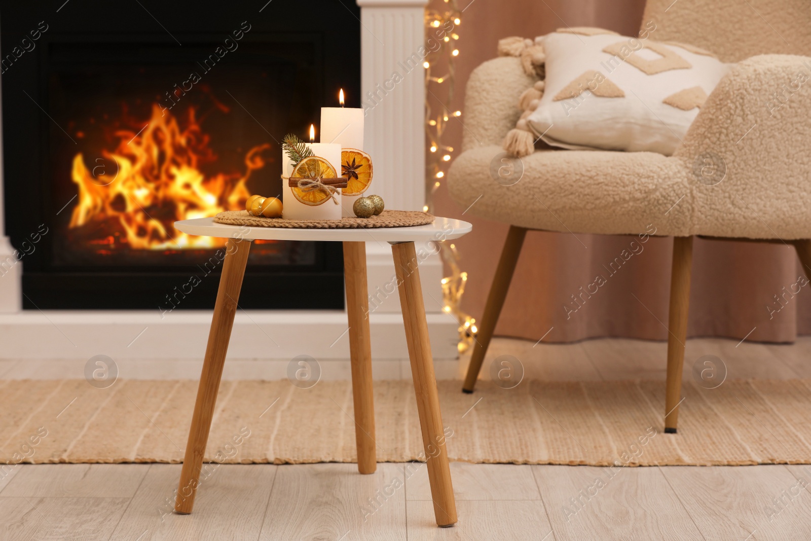 Photo of Beautiful burning candles decorated with dry orange slices and cinnamon sticks on white table in room. Christmas atmosphere