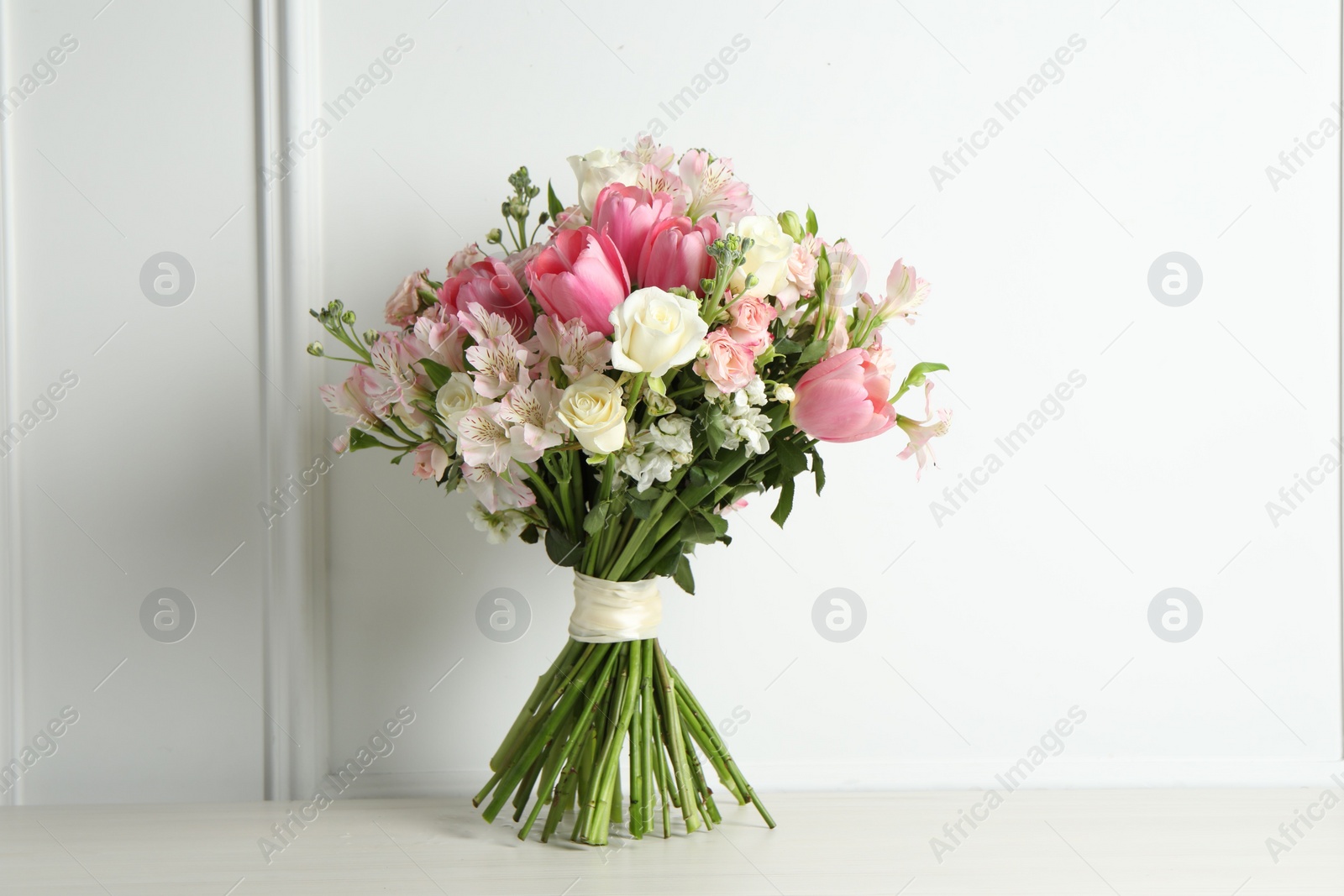 Photo of Beautiful bouquet of fresh flowers on table near white wall