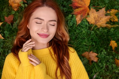 Beautiful woman lying on grass among autumn leaves, top view