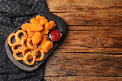 Tasty ketchup, onion rings and chicken nuggets on wooden table, top view. Space for text