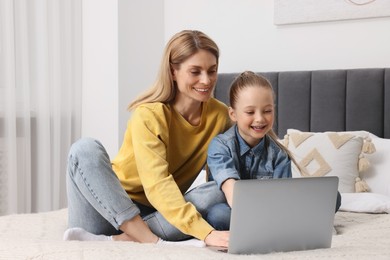 Happy woman and her daughter with laptop on bed at home